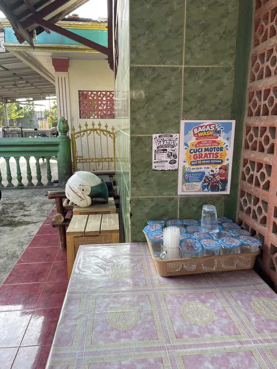 Poster promo cuci motor gratis di teras BAGAS WASH, di samping meja air minum